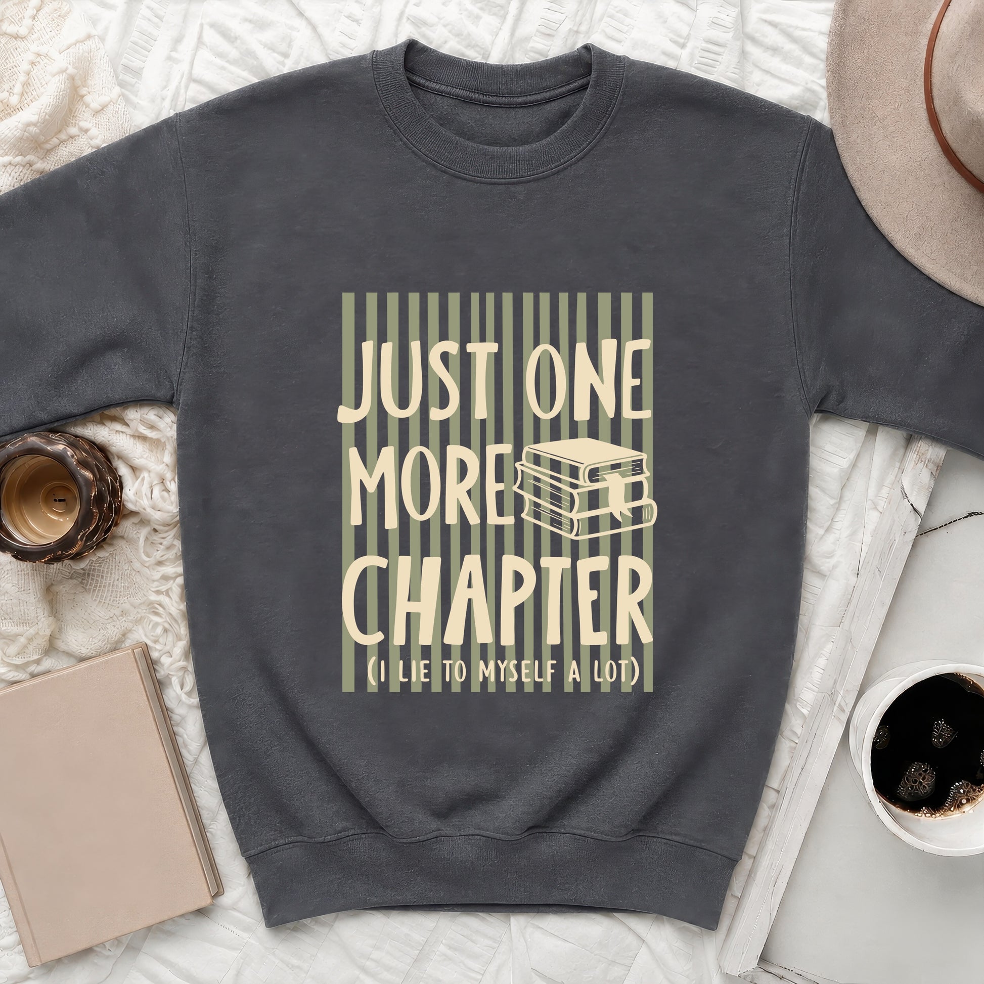 Dark grey sweatshirt with "JUST ONE MORE CHAPTER (I LIE TO MYSELF A LOT)" text and stacked books graphic.