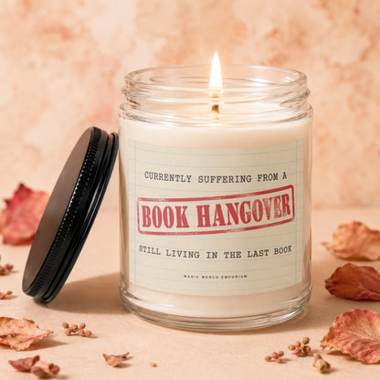 Candle with "Book Hangover" label and burning wick, surrounded by dried leaves.