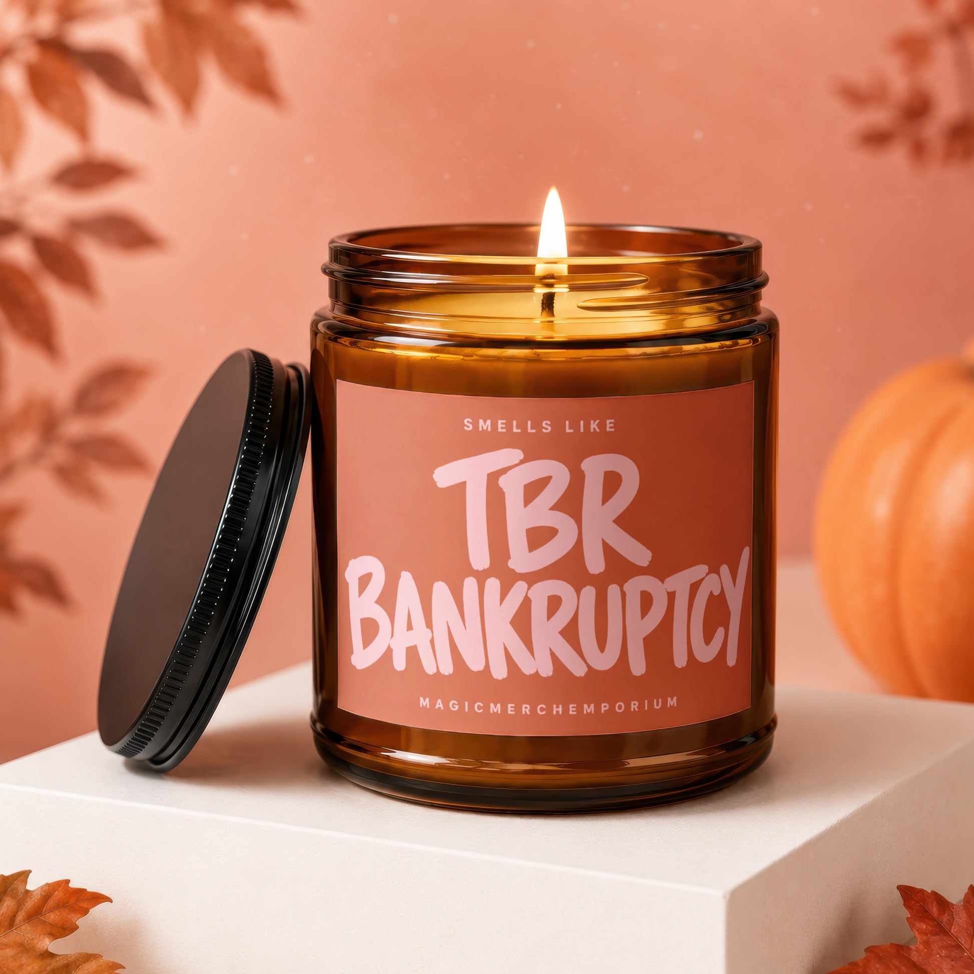 Amber candle with lit wick, black lid, and "Smells Like TBR Bankruptcy" label.