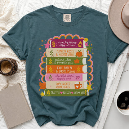 Teal t-shirt with stack of books featuring autumn phrases and graphics.