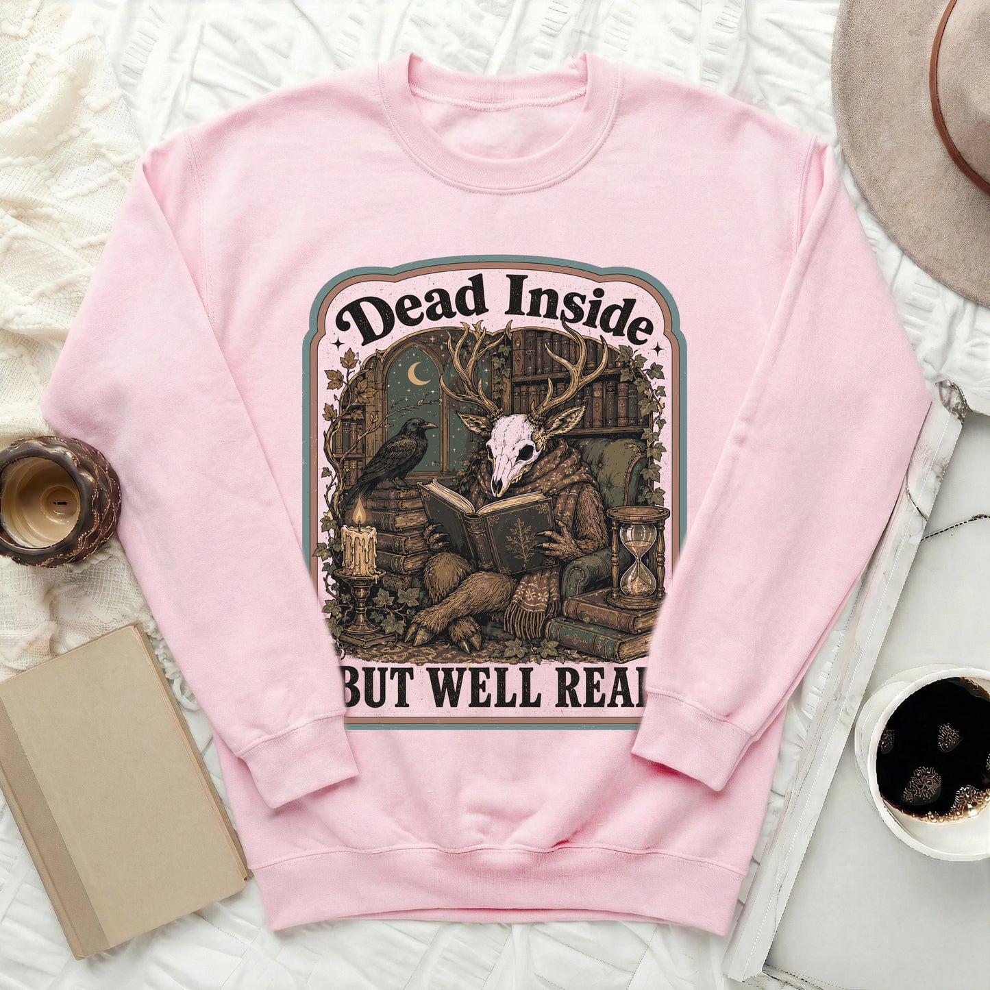 Pink sweatshirt with a graphic featuring a deer skull, books, and the text "Dead Inside But Well Read".