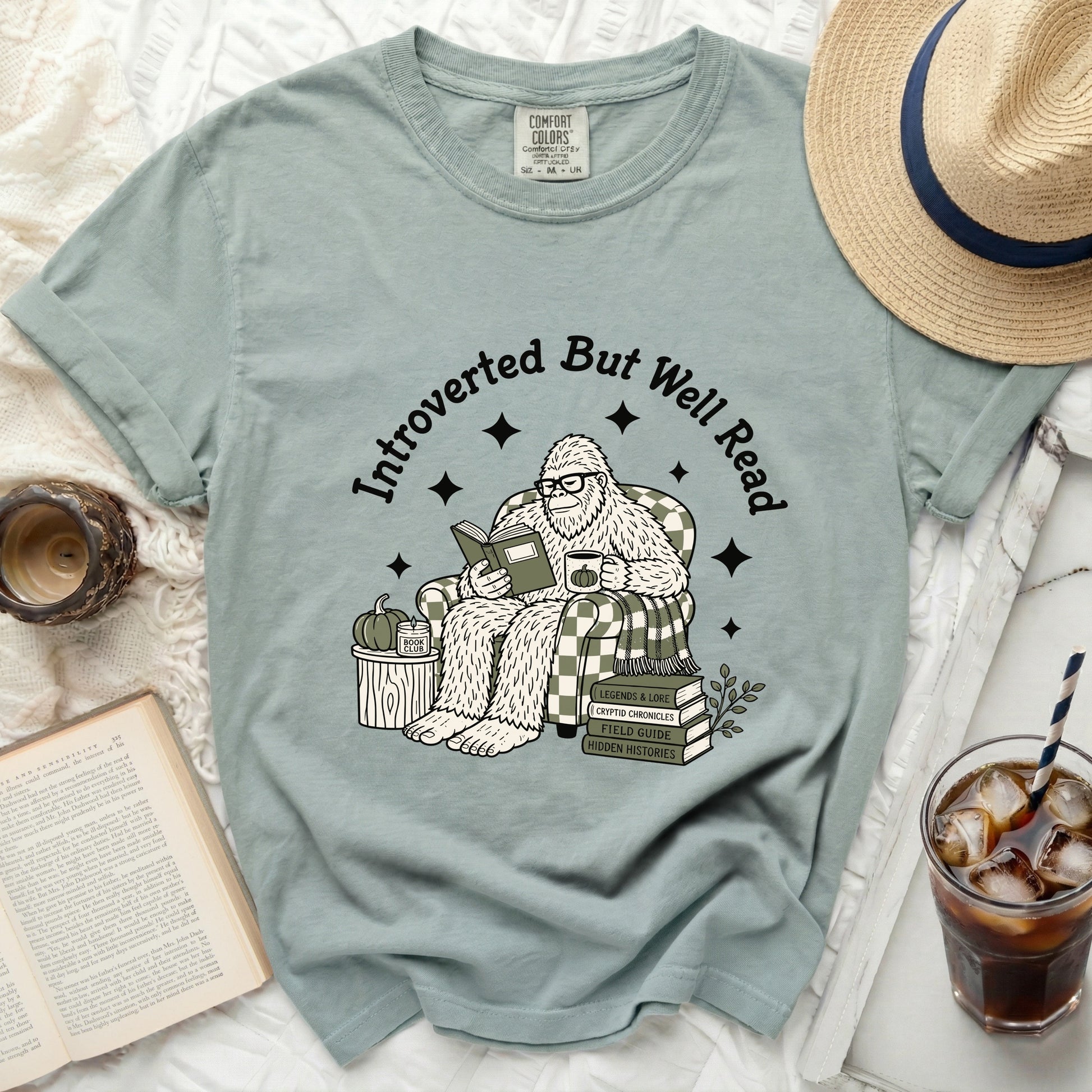 Bigfoot wearing glasses reads a book, seated in a chair with plaid pattern.