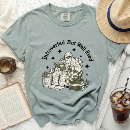 Bigfoot wearing glasses reads a book, seated in a chair with plaid pattern.