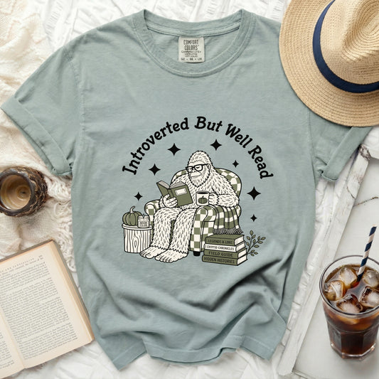 Bigfoot wearing glasses reads a book, seated in a chair with plaid pattern.