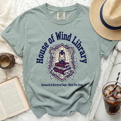 Light blue t-shirt with "House of Wind Library" and books graphic.