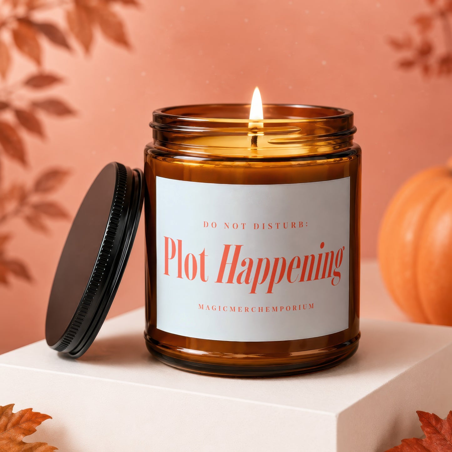 Amber glass candle with lit flame and label reading "Plot Happening".