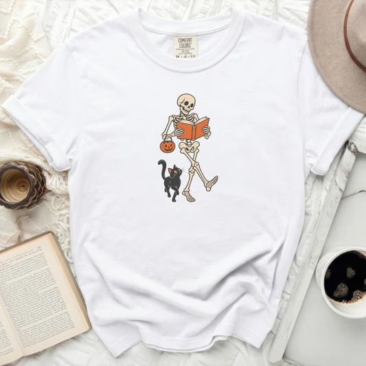 White t-shirt with skeleton reading, holding pumpkin bucket, and black cat.
