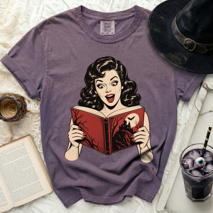 Vintage style graphic of woman reading a spooky book on a purple t-shirt.