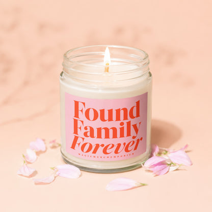 Glass jar candle with pink label reading "Found Family Forever" and a smaller text "MAGIC MERCH EMPORIUM".