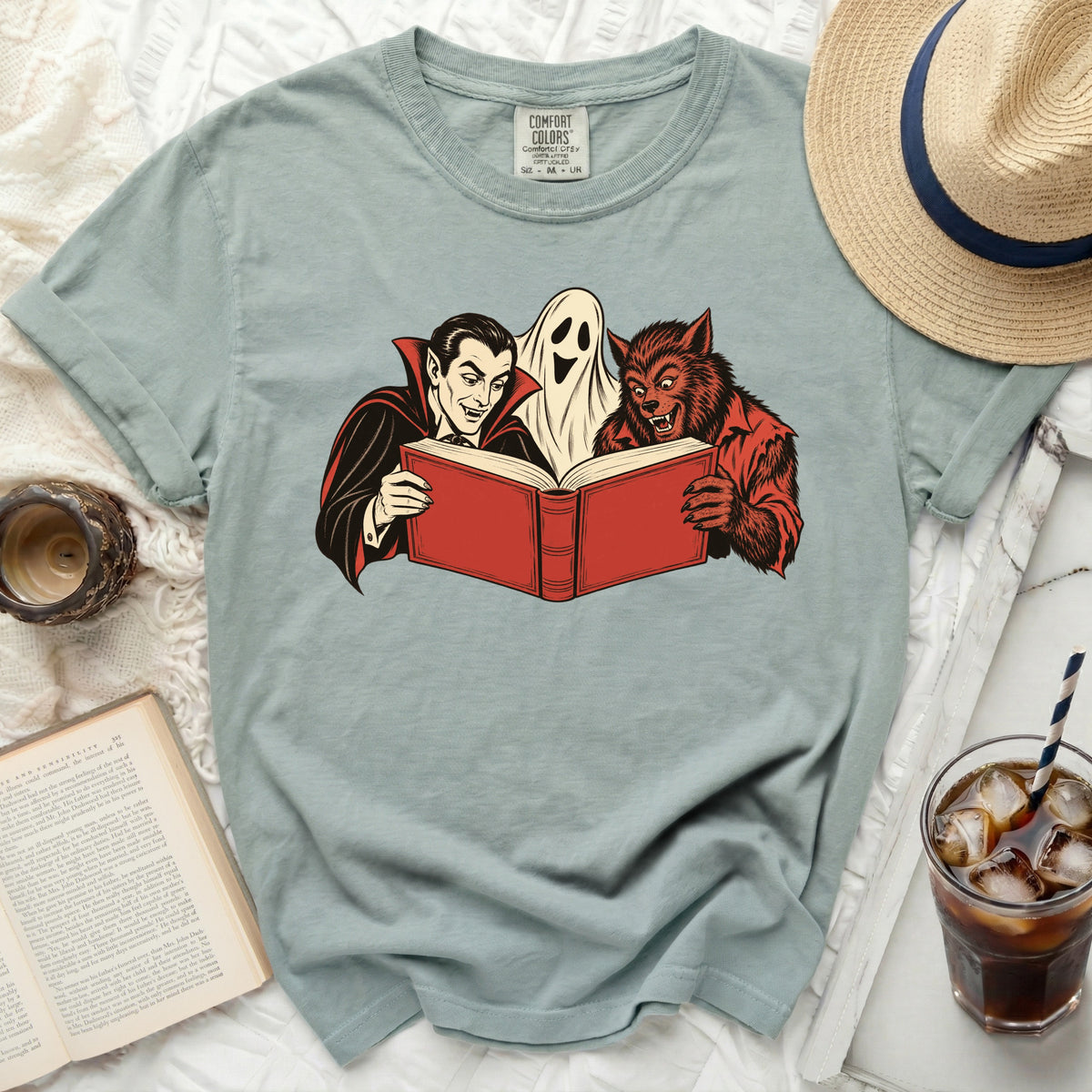 Vampire, ghost, and werewolf reading a red book graphic on a light blue t-shirt.