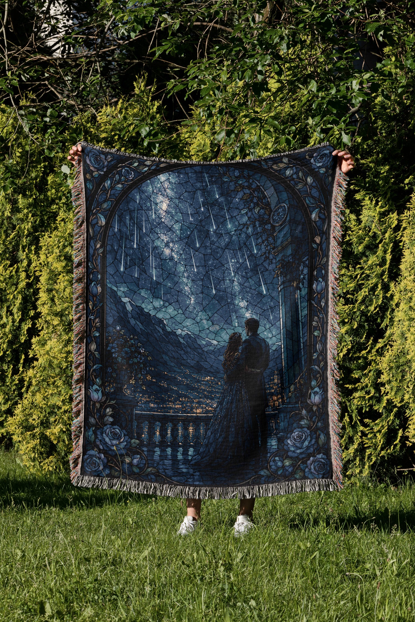 A person is holding up a large, intricately designed blanket with a scene of a couple standing together under a starry night sky.