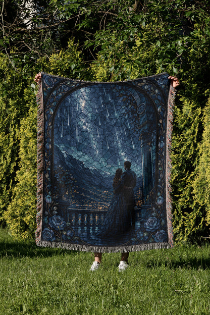 A person is holding up a large, intricately designed blanket with a scene of a couple standing together under a starry night sky.