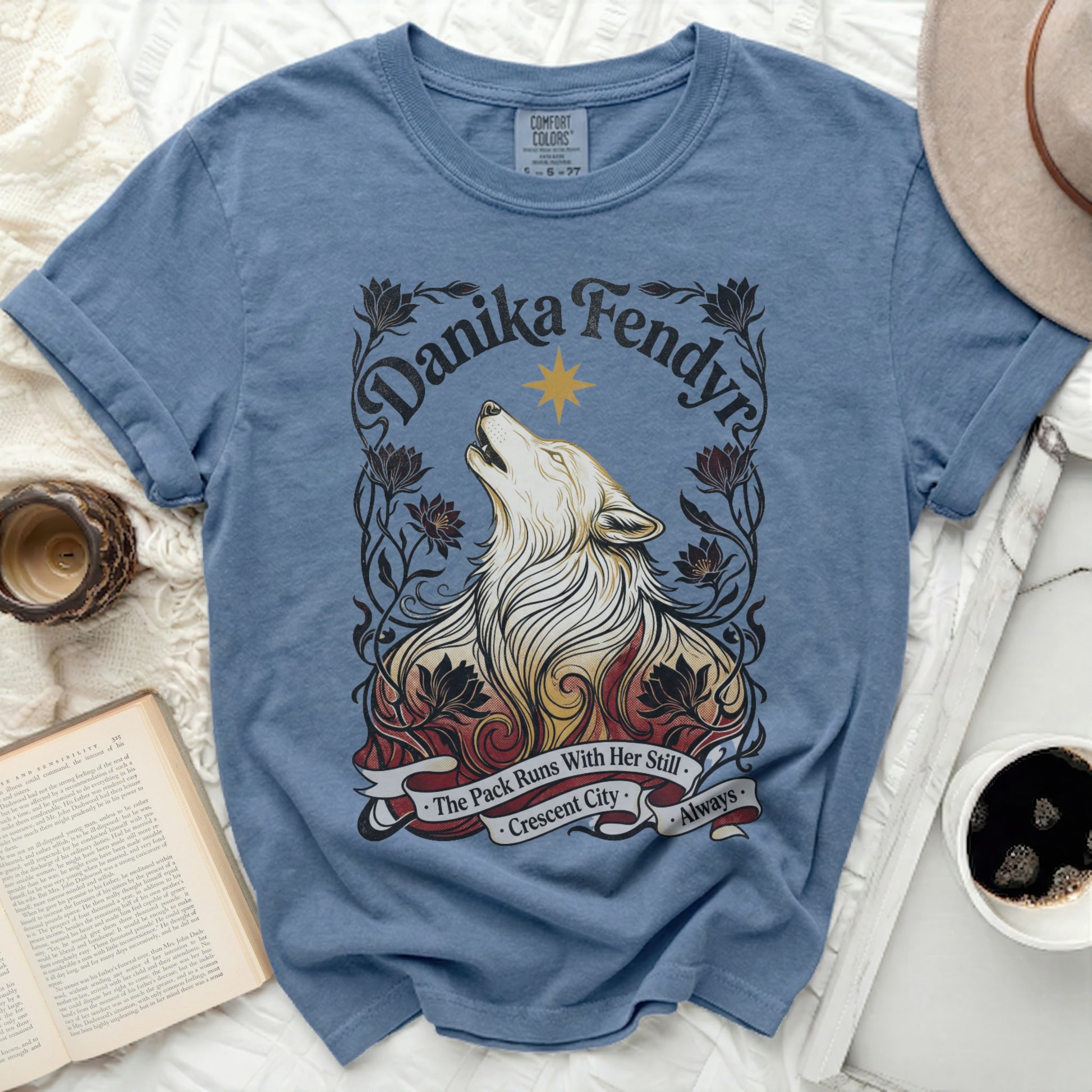 Blue t-shirt with a wolf graphic and "Danika Fendyr, The Pack Runs With Her Still, Crescent City, Always" text.