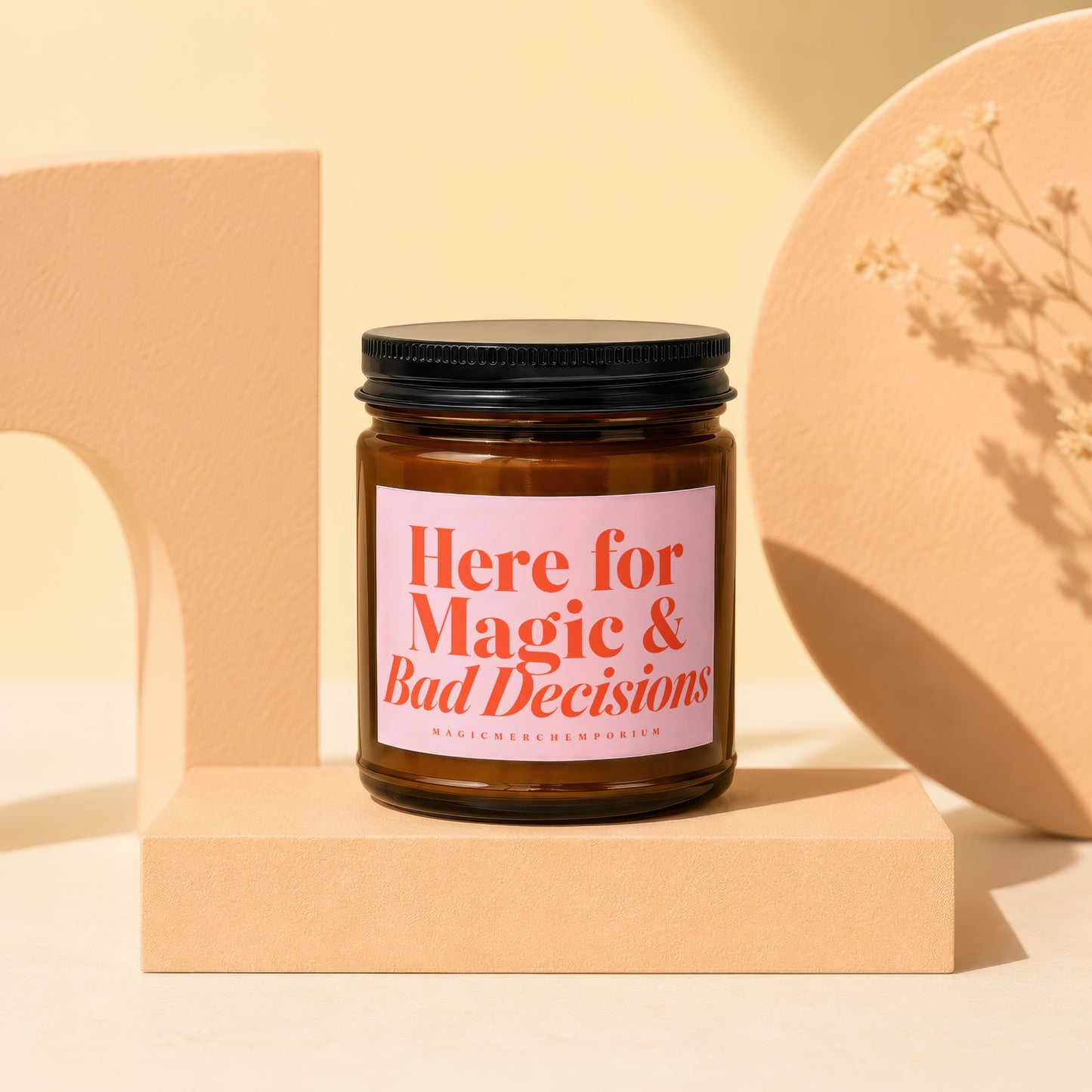 Amber glass candle with pink label reading "Here for Magic & Bad Decisions."