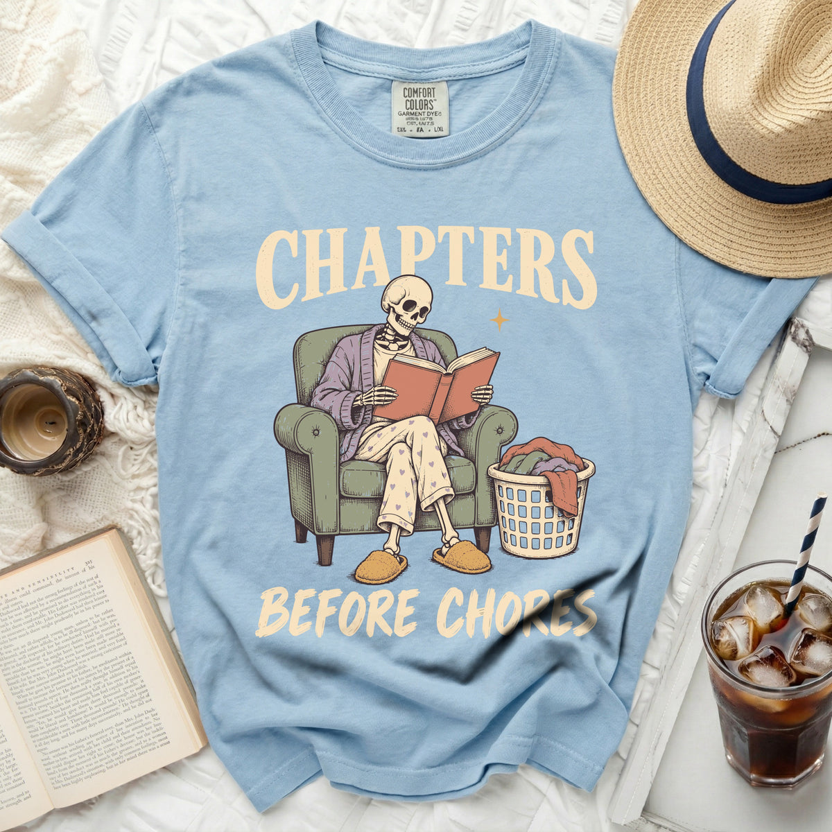Light blue t-shirt with skeleton reading a book, "Chapters Before Chores".