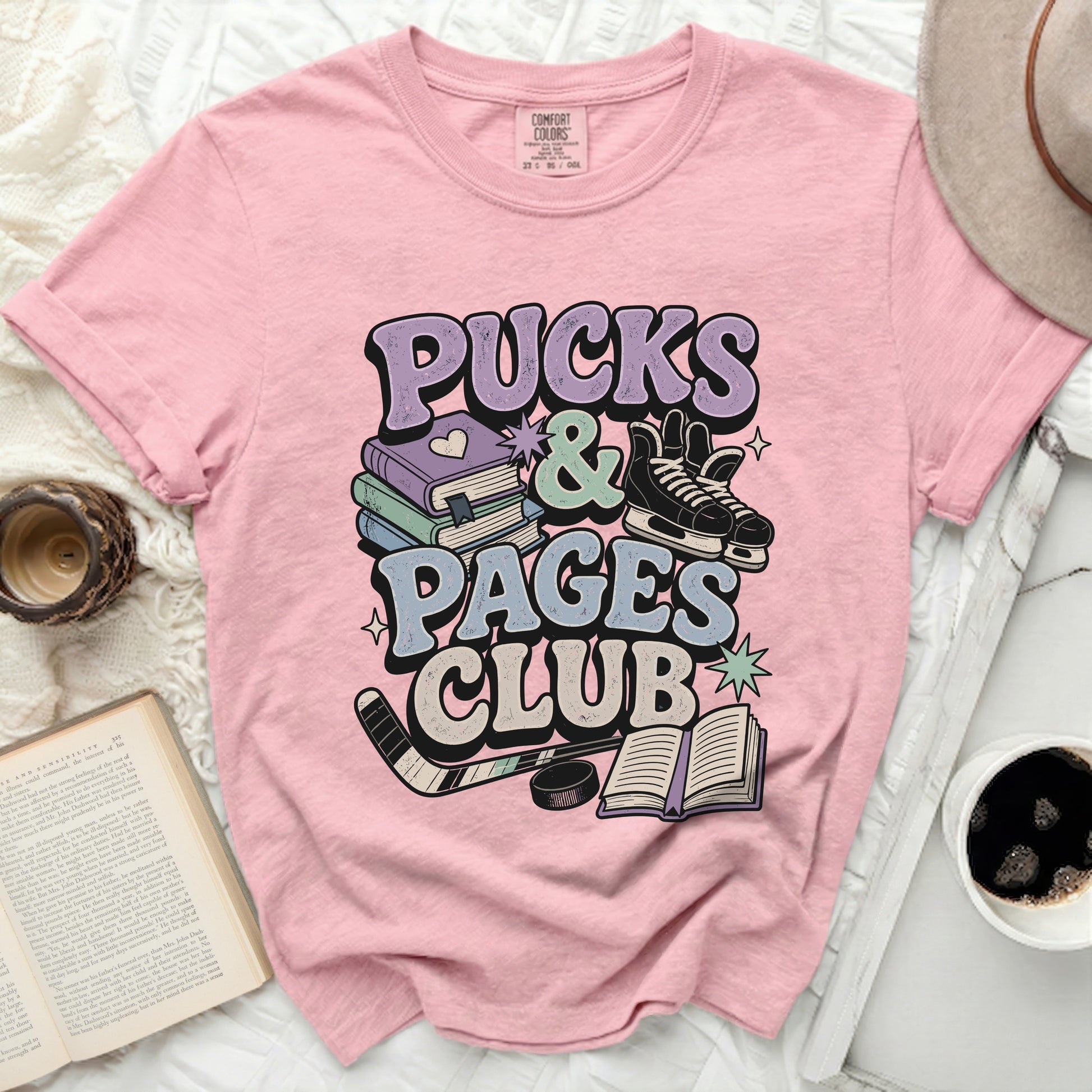Pink t-shirt with "Pucks & Pages Club" text and hockey/book graphics.