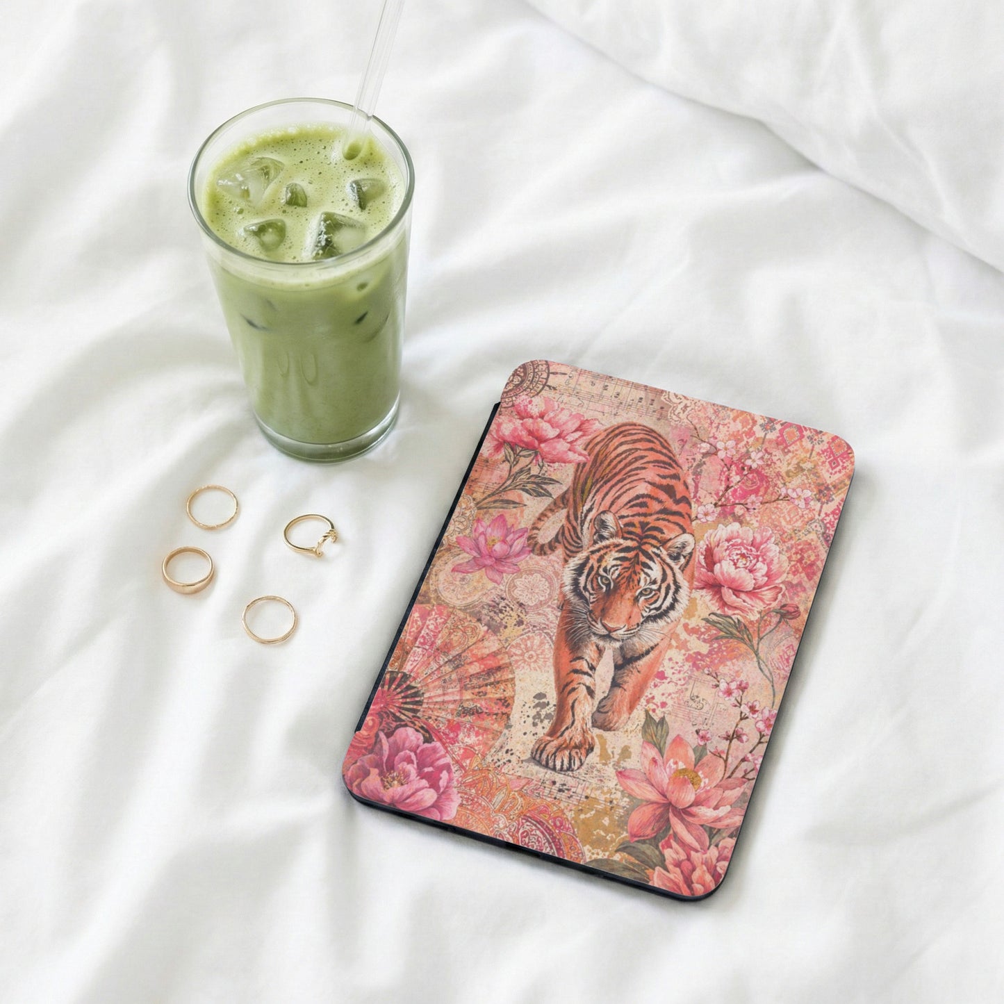 Tiger with floral pattern mousepad on white fabric, next to iced drink and rings.