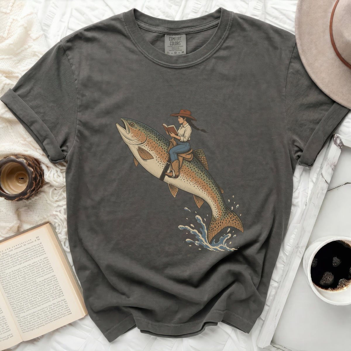Girl riding a rainbow trout, reading a book, on dark gray t-shirt.