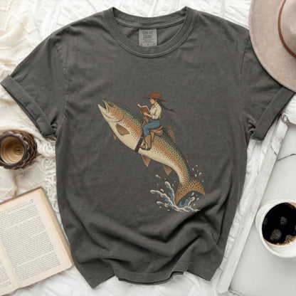 Girl riding a rainbow trout, reading a book, on dark gray t-shirt.