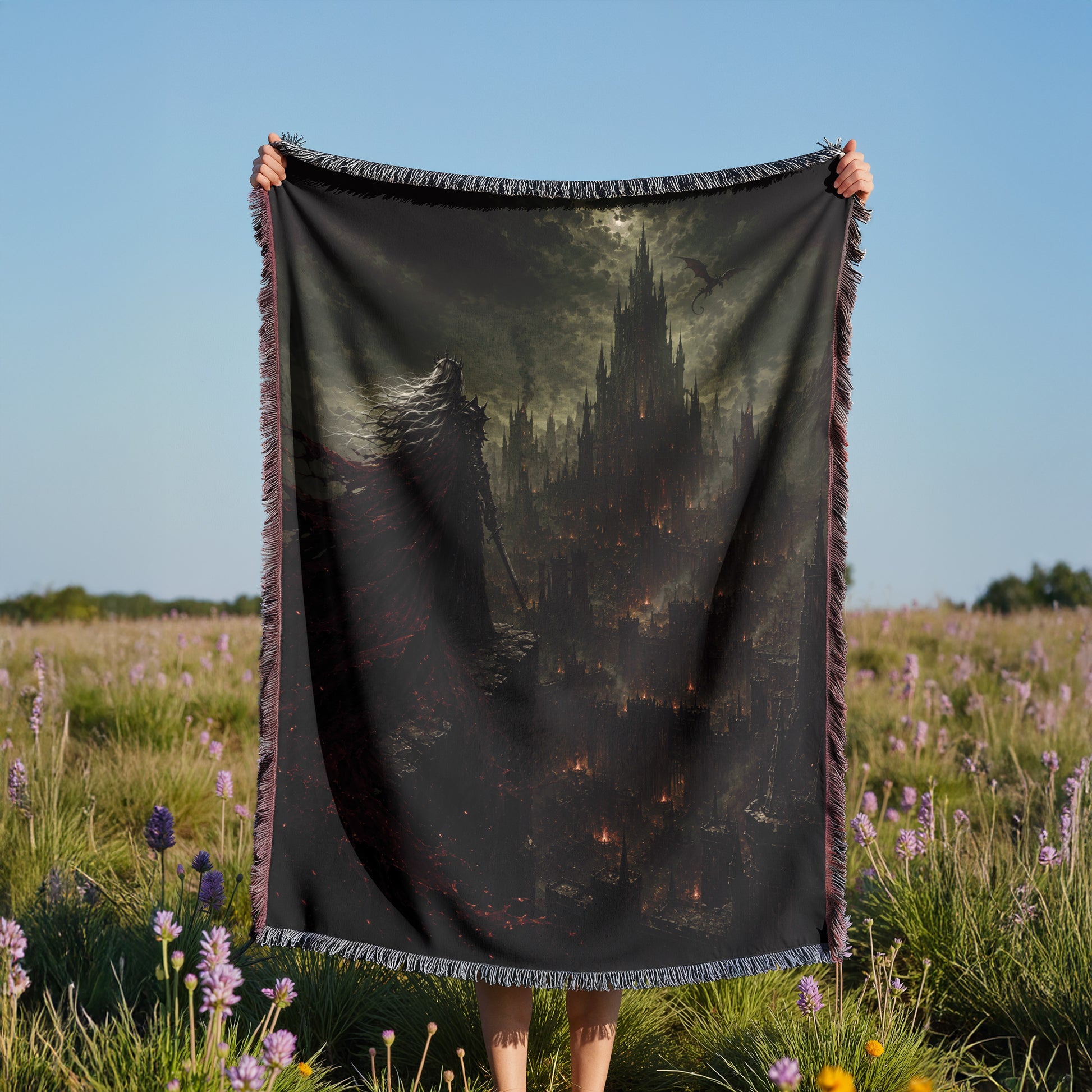 A person is holding a large black blanket with a painting of a castle on it, standing in a field with purple flowers.