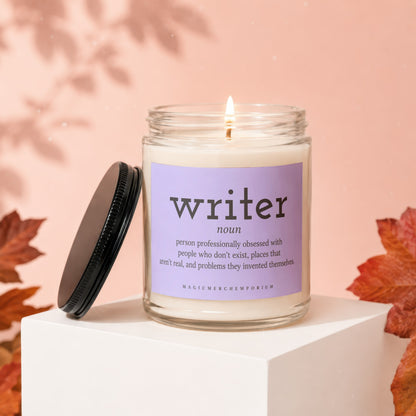Candle with "writer" definition label, lit flame, autumn leaves, and lid.