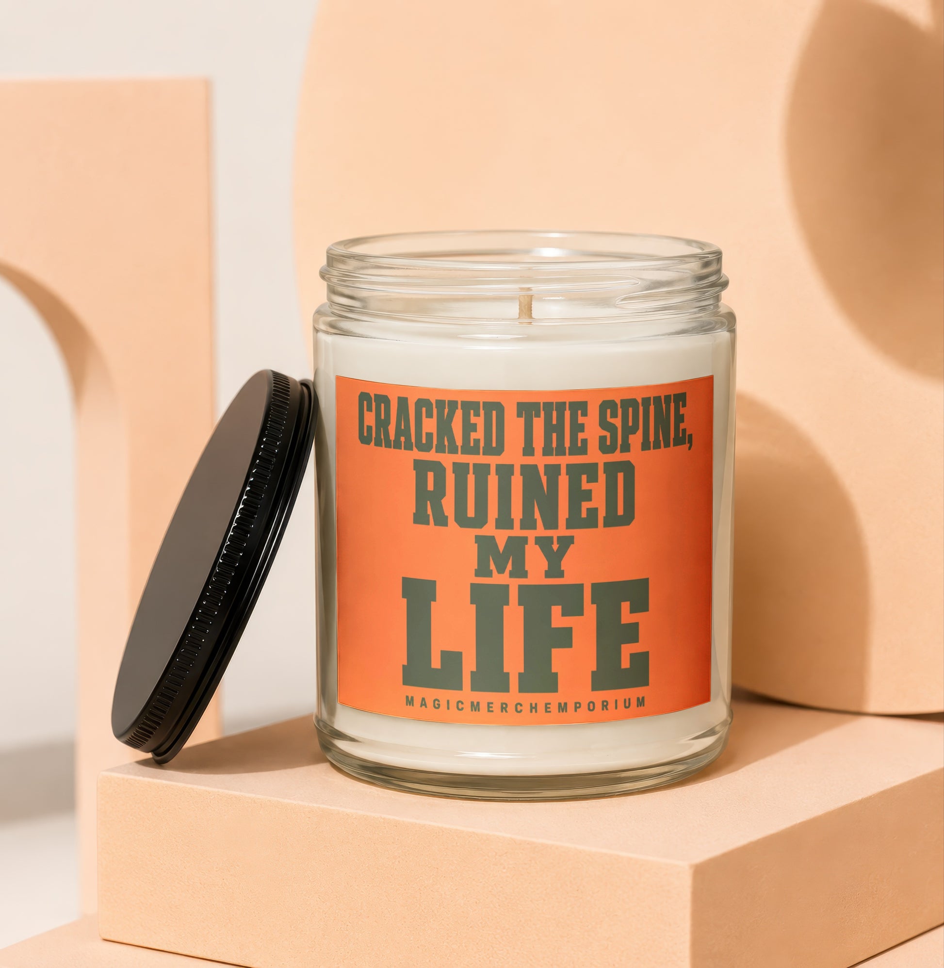 Glass candle with orange label reading "CRACKED THE SPINE, RUINED MY LIFE".