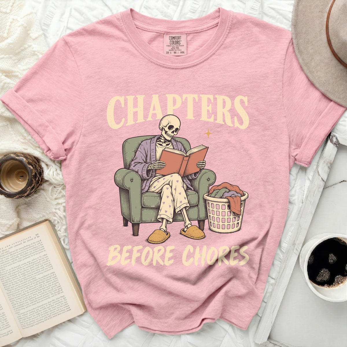 Pink t-shirt with skeleton reading book and text "Chapters Before Chores".