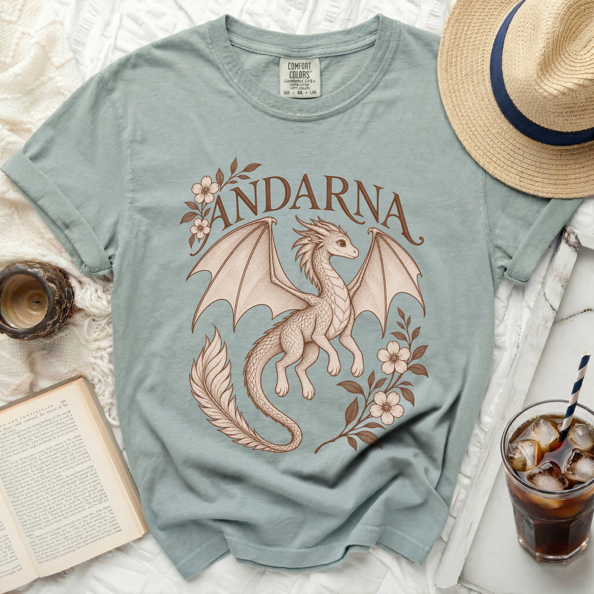 Sage green t-shirt featuring a brown illustration of a dragon, floral branches, and the text Andarna.
