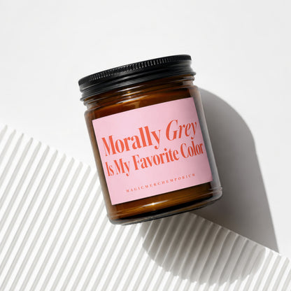 Amber jar candle with pink label reading "Morally Grey Is My Favorite Color" and "MAGICMERCHIMPORIUM"
