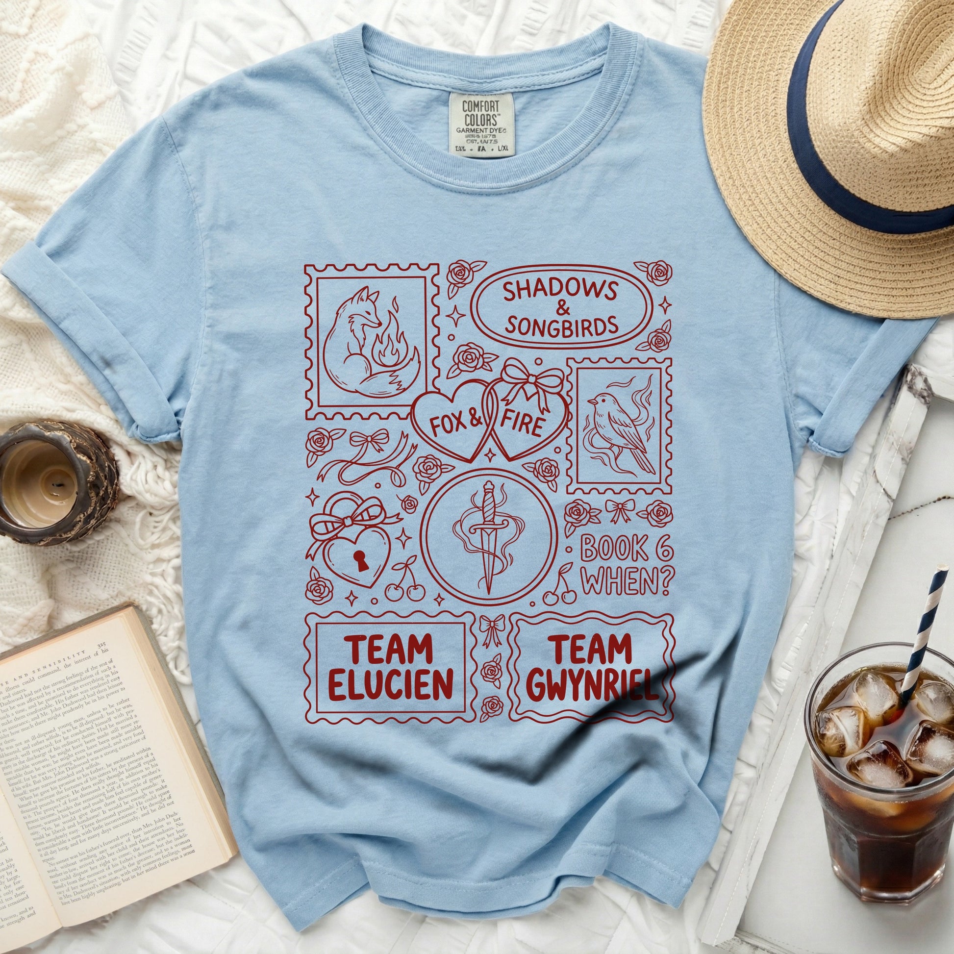Light blue t-shirt with red graphic of stamps featuring fox, songbirds, dagger, and text.