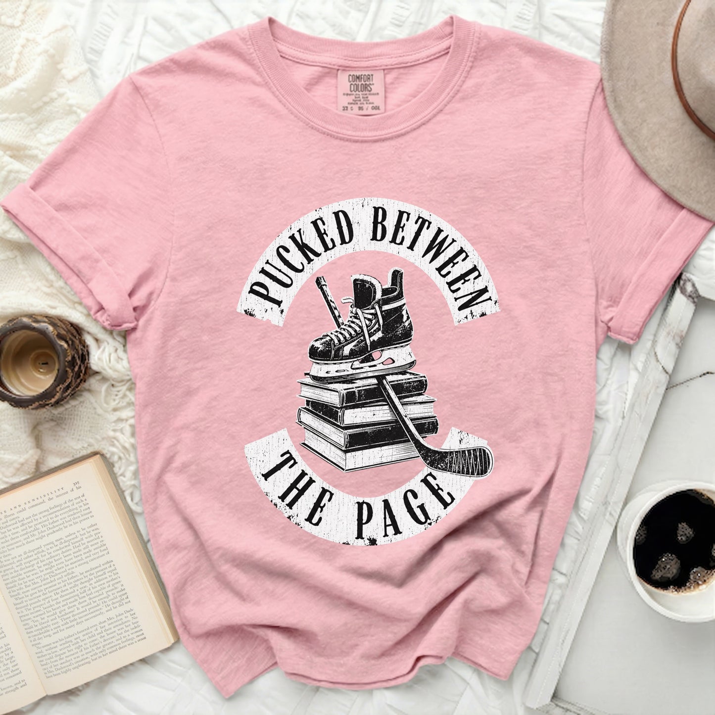 Pink t-shirt with "Pucked Between the Page" and hockey gear on books.