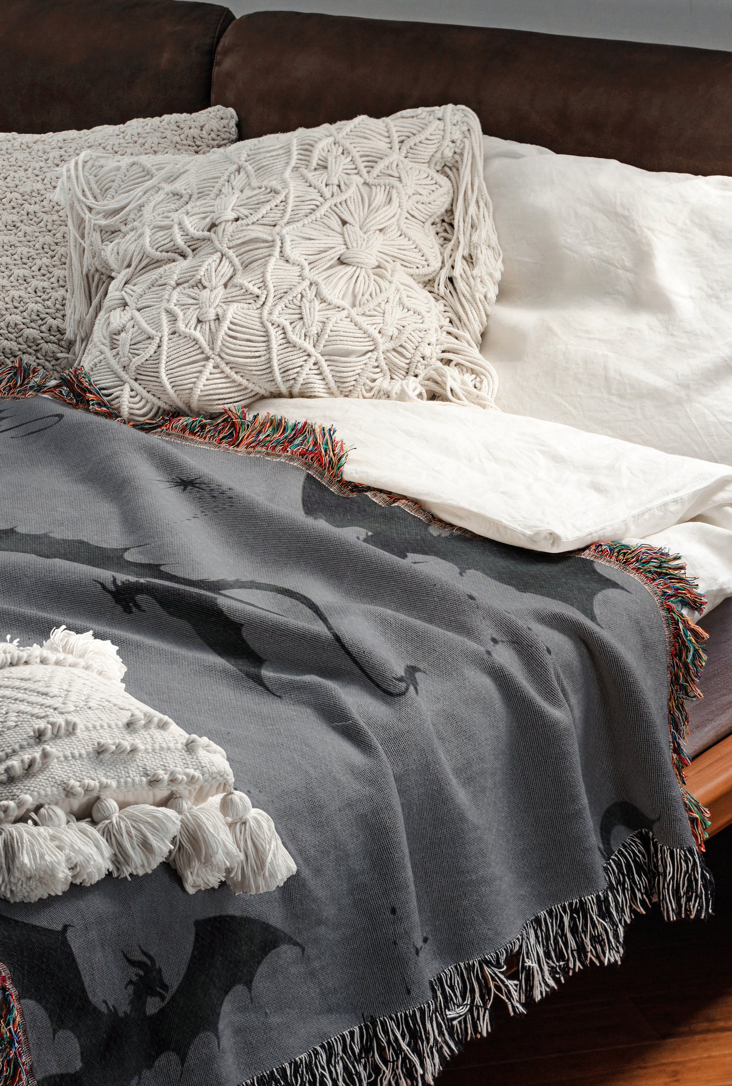 a cozy and inviting bedroom scene, featuring a bed with a gray blanket and white pillows, as well as a brown leather couch. The bed is adorned with a dragon-themed throw blanket and a white shawl, adding a touch of whimsy and warmth to the space.
