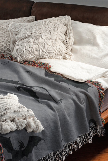 a cozy and inviting bedroom scene, featuring a bed with a gray blanket and white pillows, as well as a brown leather couch. The bed is adorned with a dragon-themed throw blanket and a white shawl, adding a touch of whimsy and warmth to the space.
