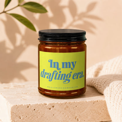 Amber candle with a lime green label reading "In my drafting era."
