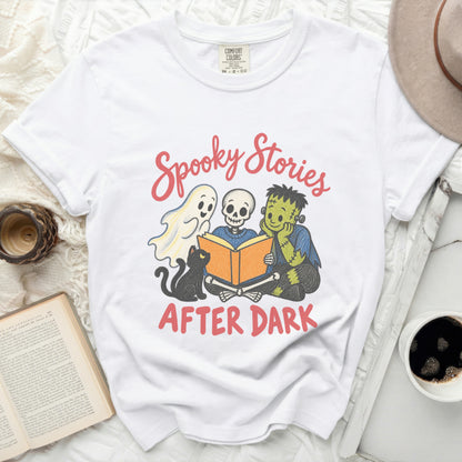 White t-shirt with "Spooky Stories After Dark" graphic of ghost, skeleton, and Frankenstein reading.