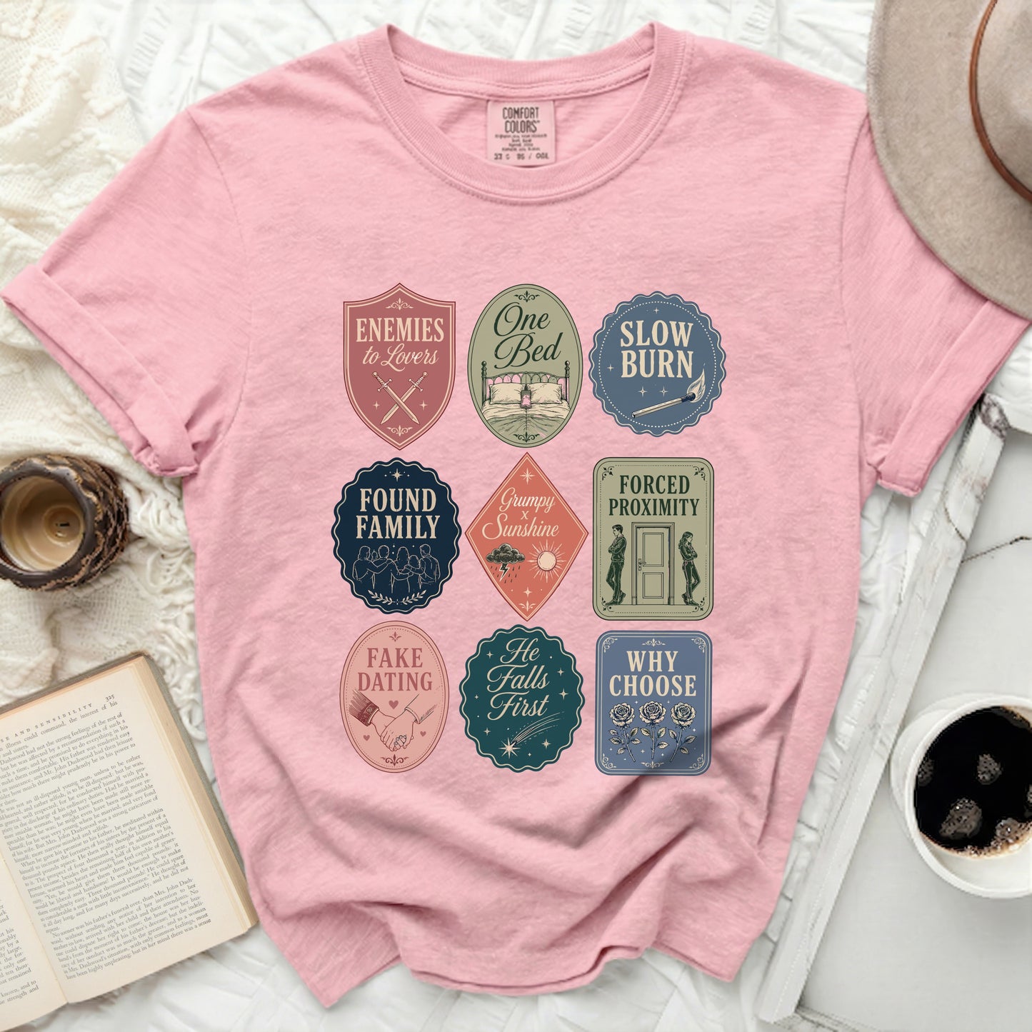 Pink t-shirt with nine retro badges featuring phrases like "Enemies to Lovers" and "Slow Burn".