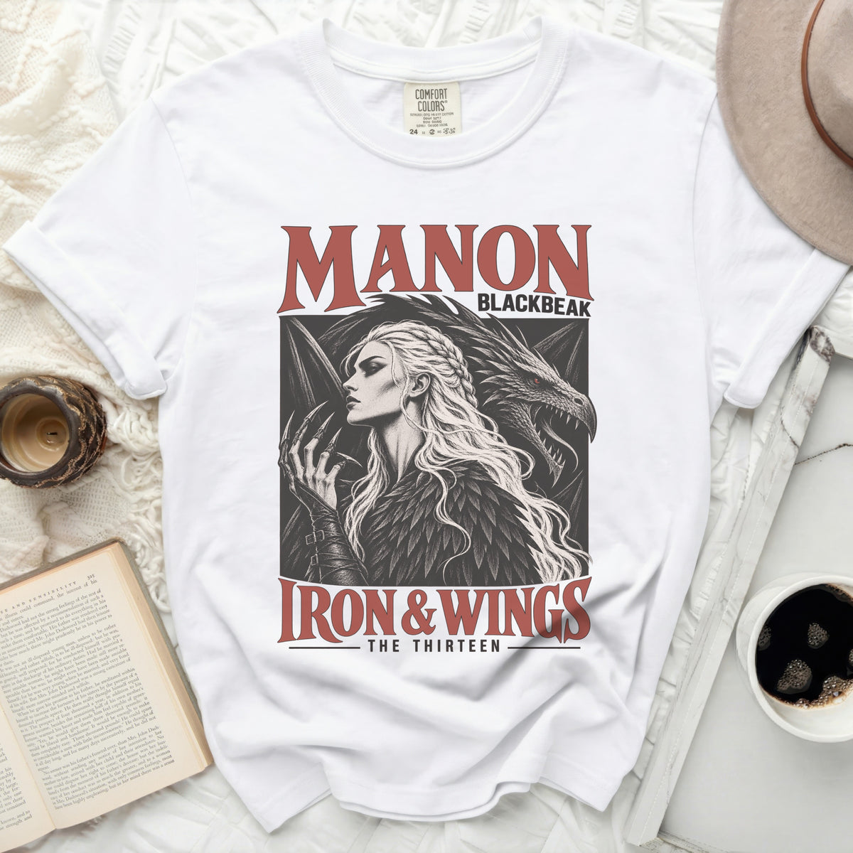 White t-shirt with "MANON BLACKBEAK IRON & WINGS THE THIRTEEN" graphic.