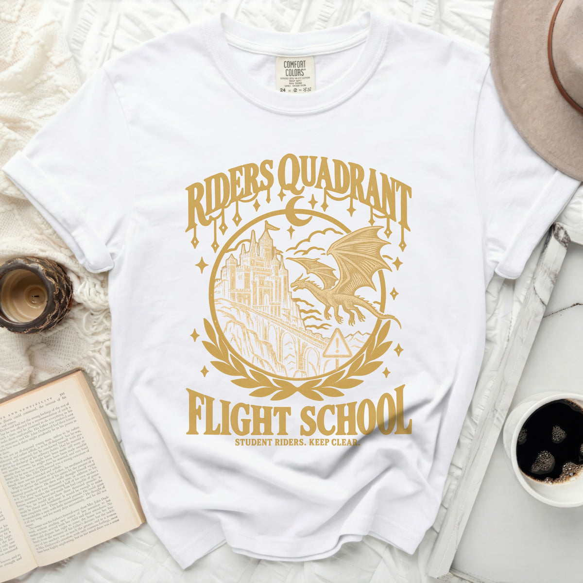 White t-shirt with gold graphic of castle, dragon, and "Riders Quadrant Flight School".