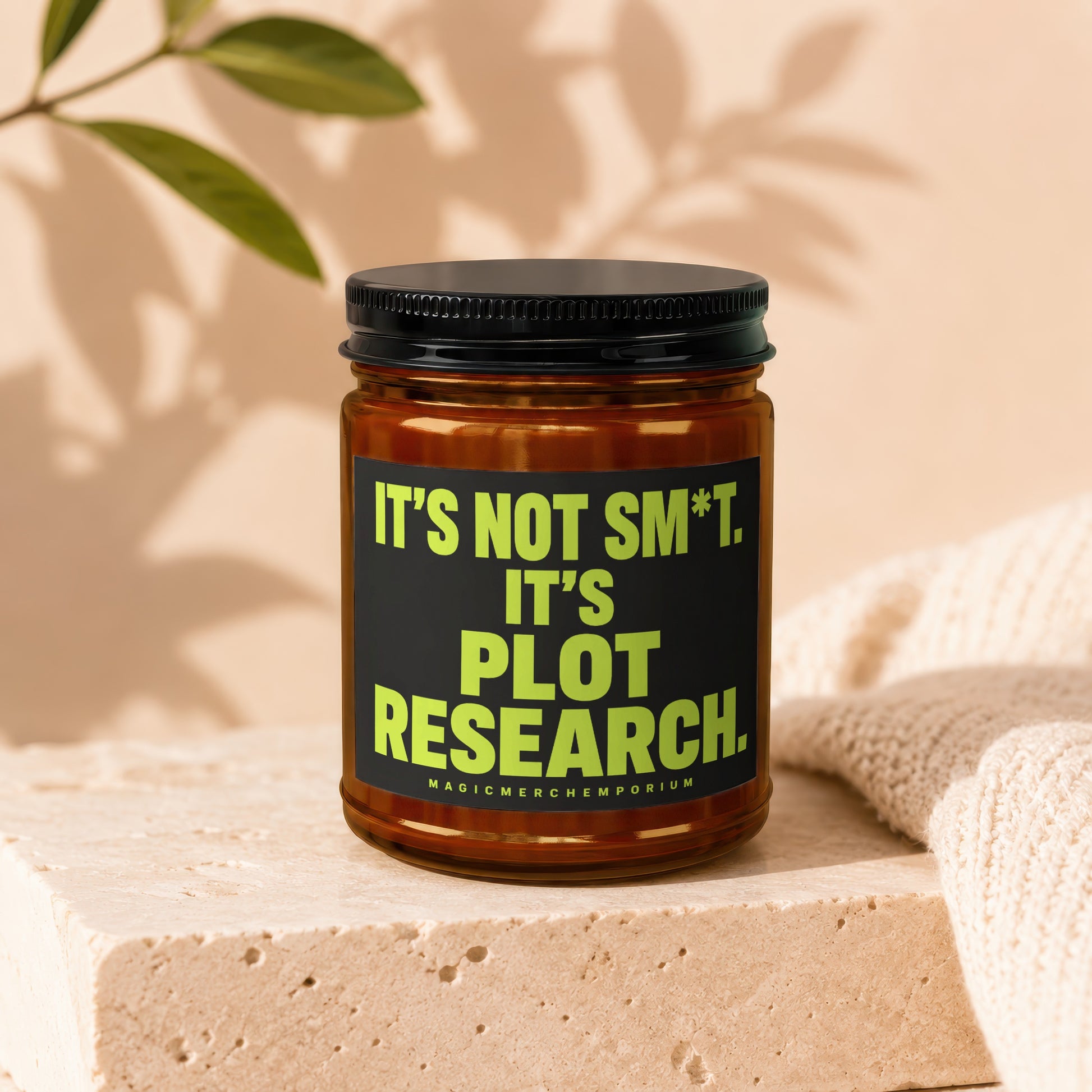 Amber jar candle with black lid and label reading "It's Not Sm*t. It's Plot Research."