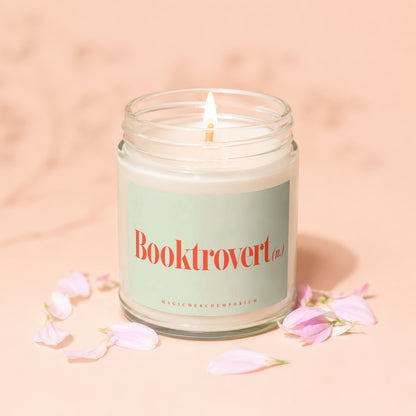 Glass jar candle with "Booktrovert" text and pink petals on a peachy background.