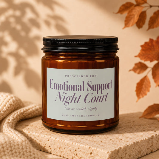 Amber jar candle labeled "Emotional Support Night Court" on textured block with knit fabric.