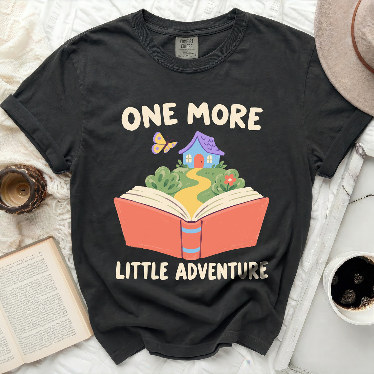 Black t-shirt with "One More Little Adventure" text and book graphic.