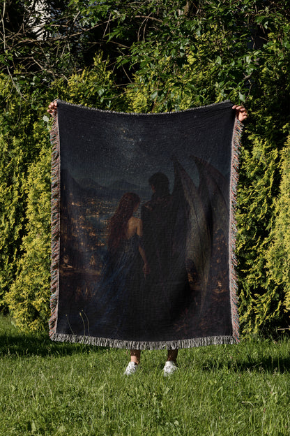 A person is standing in a grassy area, holding up a large, dark-colored blanket that features a painting of a couple.