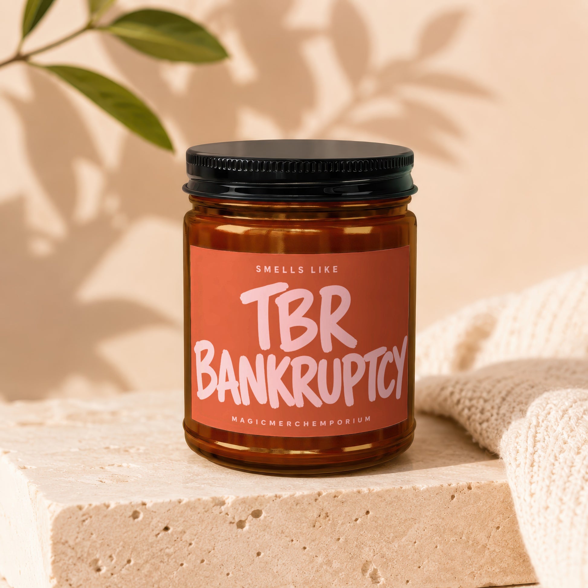 Amber jar candle with a pink label reading "TBR BANKRUPTCY" and "MAGICMERCHMEPOTRIUM".