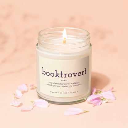 Glass jar candle with "booktrovert" definition and pink petals on a light peach background.