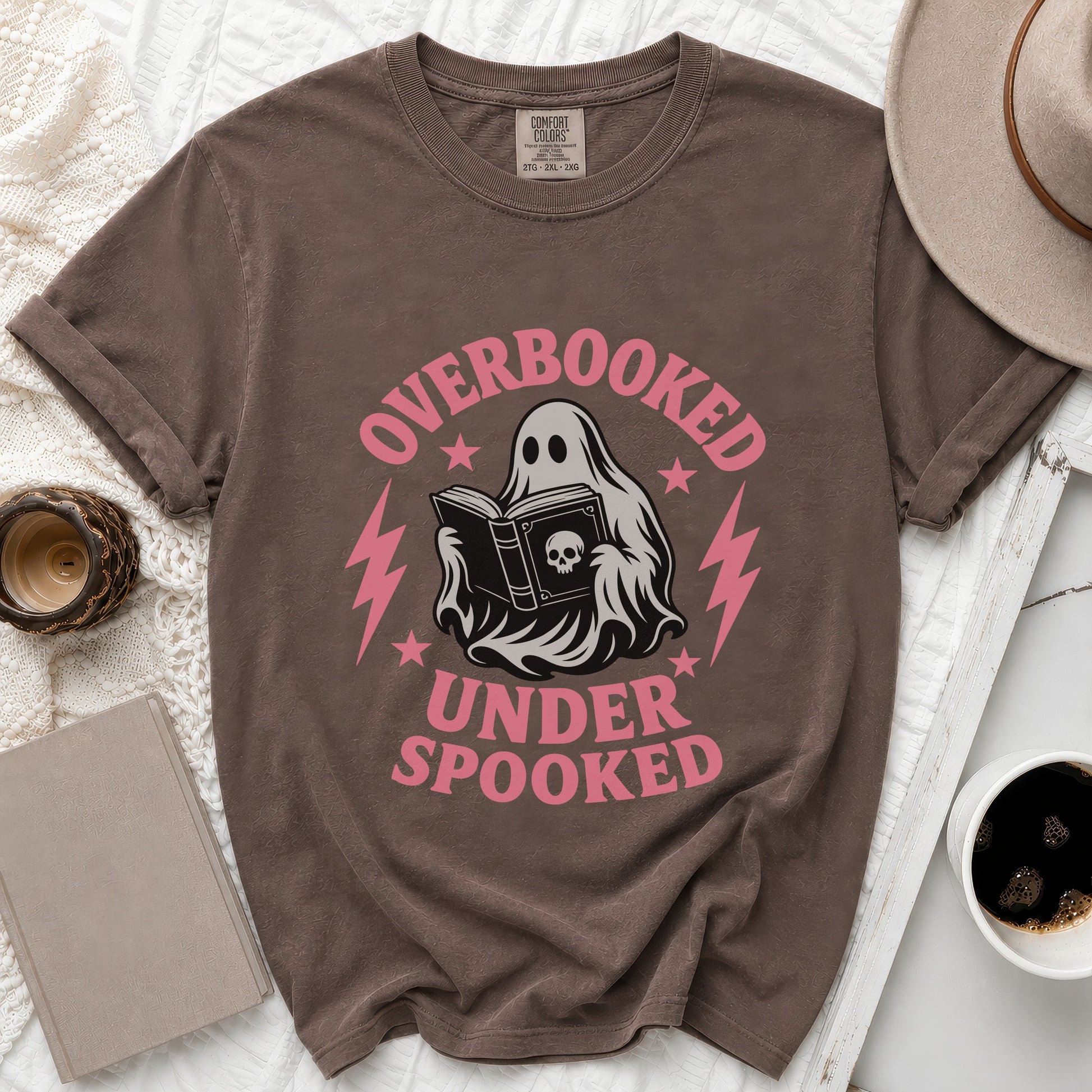 Brown t-shirt with pink text "OVERBOOKED UNDER SPOOKED" and a ghost reading a book.