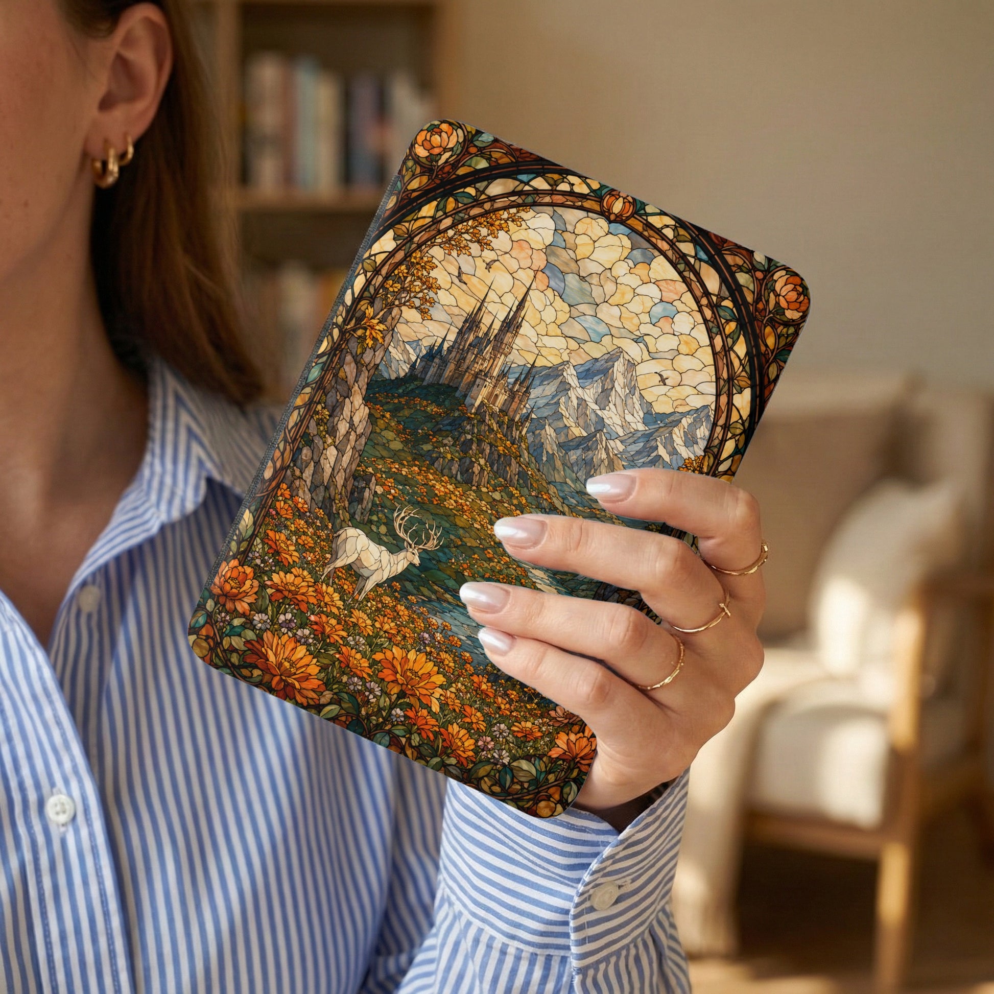 A journal with a stained-glass deer and castle art design held by a woman.