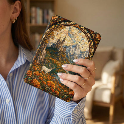 A journal with a stained-glass deer and castle art design held by a woman.