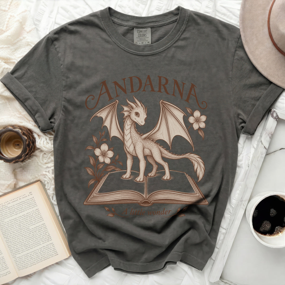 Dark grey t-shirt with a drawing of a dragon on an open book and text "ANDARNA A little wonder".