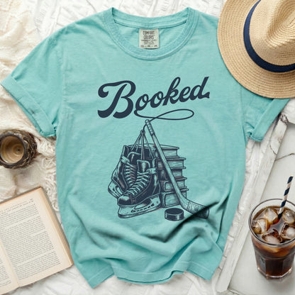 Aqua t-shirt with "Booked" text and hockey skates, stick, and puck illustration.